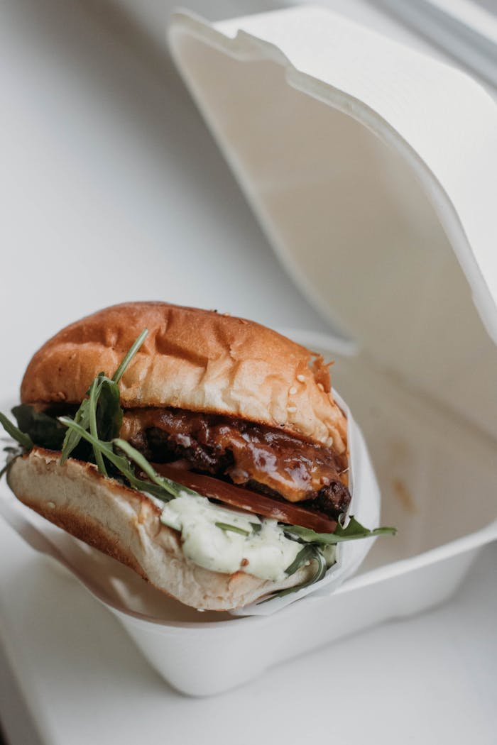 Delicious gourmet burger with arugula and sauce in a takeaway box.